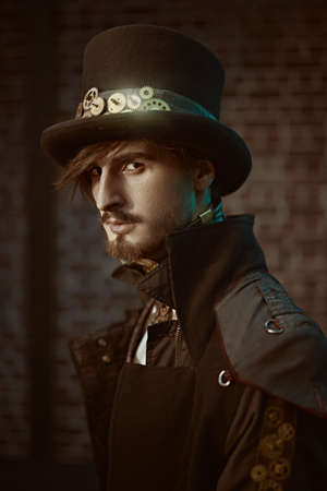 Steampunk world. Portrait of a stylish steampunk man in a coat and top hat on a brickwall background.の写真素材
