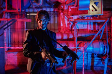 Courageous action hero with automatic guns in an industrial zone at night. Handsome wounded man special agent.の写真素材