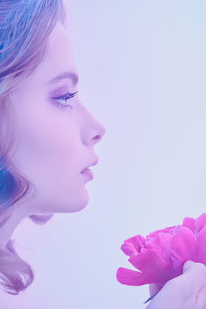 Close-up sideview portrait of a beautiful young woman with gentle lilac-violet make-up holding a delicate peony flower. Beauty, perfumery and cosmetics.の写真素材