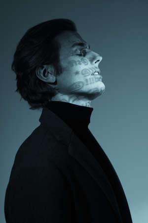 Monochrome portrait of a concentrated handsome man with symbols on face closing his eyes posing at studio. Shadows lettering fashion on his face.の写真素材