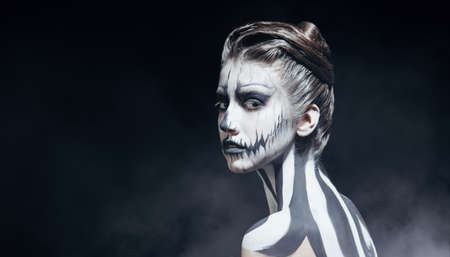 Beautiful young woman with pumpkin skull makeup over black background. Halloween. Day of The Dead. Copy space. Side and back view.の写真素材