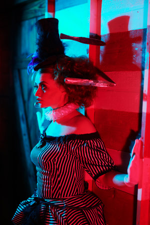 Circus performer in a clown costume performs a knife throwing trick. The dark circus concept. Retro...
