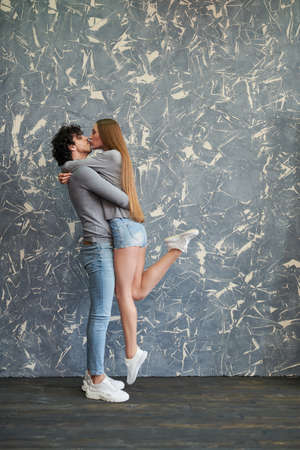 Full length portrait of a beautiful couple of young people in casual clothes kissing and hugging on a grunge backgroundの写真素材