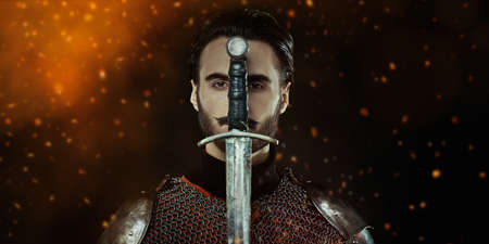 Close up portrait of a medieval knight with sword and armor on a black background with sparks of fire.の写真素材