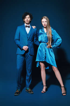 Beautiful couple of young people in love pose on a dark blue background. Full length portrait. Elegant evening fashion.の写真素材