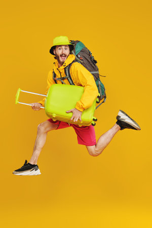 Full length portrait of emotional young hipster man jumping with backpack and suitcases. Tourism and...
