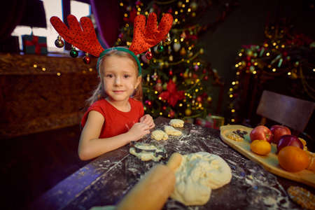 Funny little girl bakes cookies for Christmas. Happy family holidays. Child at home beautifully decorated for Christmas.の写真素材