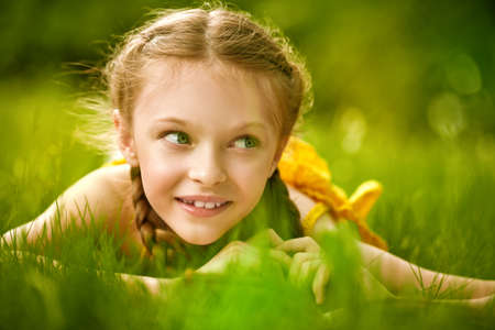 Portrait of a cute girl with pigtails lying on a green lawn and smiling. Happy summer holidays. Walk in the park.の写真素材