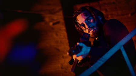 Courageous action hero with automatic guns in an industrial zone in red and blue lighting at night. Handsome wounded man.の写真素材