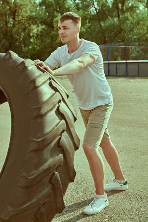 Active healthy lifestyle. Handsome muscular man is training with big tire at outdoor. Strength...