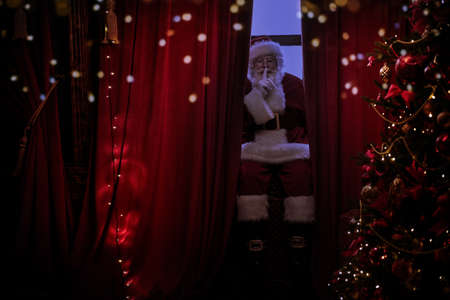 Jolly Santa Claus sneaks into the house through the window, he is sitting on the windowsill and resting. Christmas and New Year concept.の写真素材