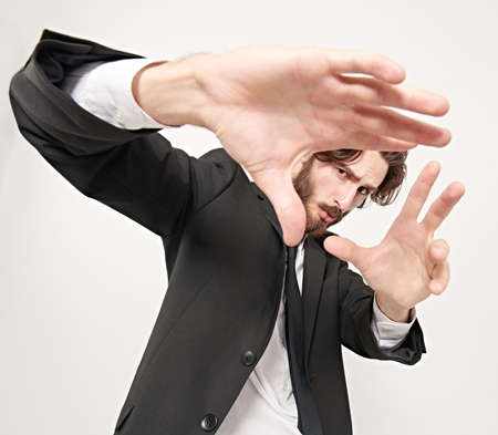 Fashion shot. Handsome male model looks at the camera through his fingers, as through a lens. Studio portrait on a white background.の写真素材