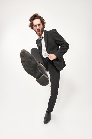 Full length portrait of a handsome well-groomed man fashion model who steps on the camera with aggression and shouts. Fashion concept. Emotions. White background.の写真素材