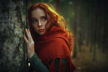 Portrait of beautiful red haired girl in a traditional green celtic dress and a red cloak is in forest. Historical reconstruction of ancient Celtic times.の写真素材