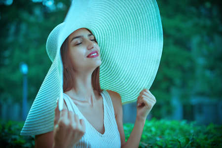 Portrait of a smiling girl in a summer outfit and a wide-brimmed hat with her eyes closed.の写真素材