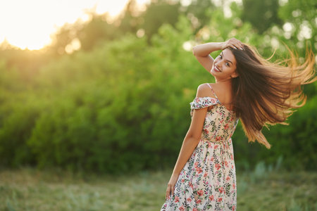 Happy young woman poses on the move in a summer floral dress in the park. Summer fashion and beauty.の写真素材