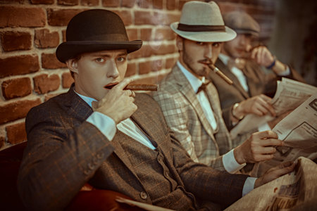 Three handsome men in elegant suits sit on a leather sofa, smoke cigars and read newspapers....