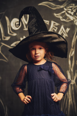 Happy cute girl in carnival costume of a witch on a Halloween background.