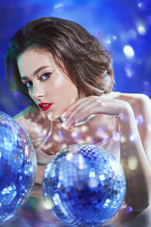 Stunning young woman with evening make-up and hairstyle poses in jewelry with gems in the glow of...