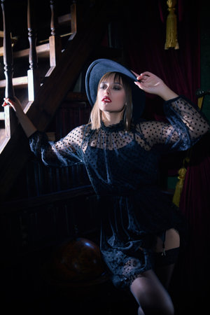 Attractive brunette girl in a black evening dress and black lace stockings allures in a luxury...