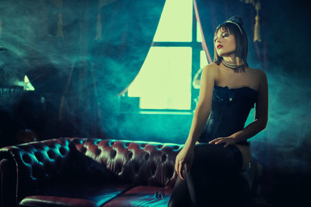 Sexy woman in black underwear and red hat allures on the sofa surrounded by cigarette smoke.