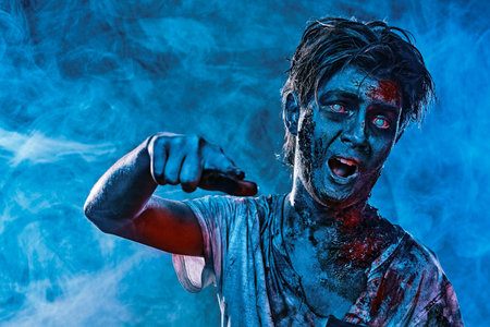 Halloween. Portrait of an aggressive scary zombie boy teenager in smoke in blue lighting. Horror...