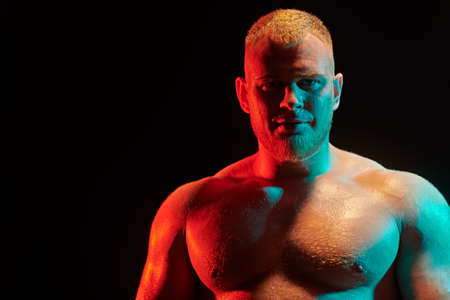 Portrait of a strong redhead athletic man on black background in multicolour lighting with copy space. Male beauty concept.の写真素材