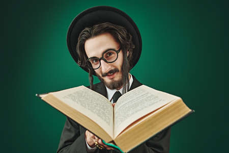 Portrait of happy orthodox Jewish man holding opened talmud in his hands. Studio shot on a green background.の写真素材