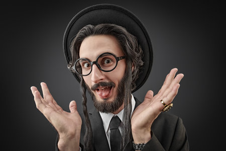 Portrait of a comical Orthodox Jewish man making faces and spreads his hands. Studio shot on a dark...