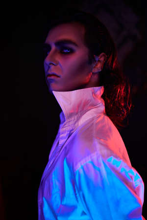 Portrait of a handsome young aristocrat vampire looking arrogantly to the camera in crimson and blue lighting in darkness.の写真素材