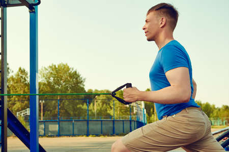 Working out at outdoor gym. An athletic man does strength exercises with elastic bands against the blue sky. Active healthy lifestyle.の写真素材