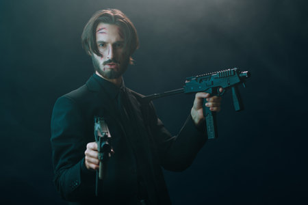 Brave special agent in a black suit with automatic guns in his hands on a dark foggy background.