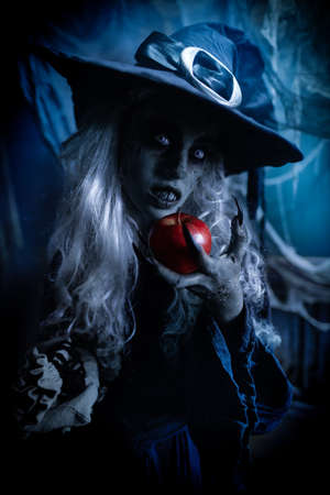 Halloween. Portrait of an ugly old witch standing with her magic staff on a black background surrounded by sparks of fire. Witchcraft.の写真素材