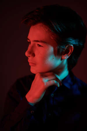 Portrait of a serious handsome boy teenager standing in the dark in red light and looking away thoughtfully. People, emotions. Studio portrait.の写真素材