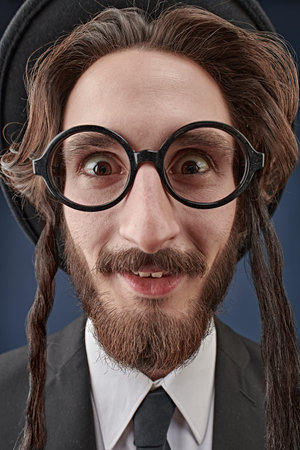 Portrait of a comical Orthodox Jewish man making faces. Studio shot on a dark blue background.