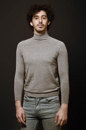 Handsome young man with curly dark hair poses in casual clothes on a black background. Men's beauty.の写真素材