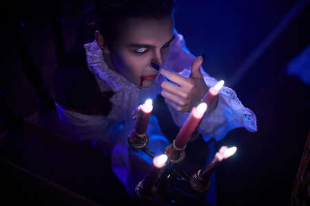 Scary vampire grins at a candle sneaking around the castle in the night in search of a victim. 19th century style. Halloween.の写真素材