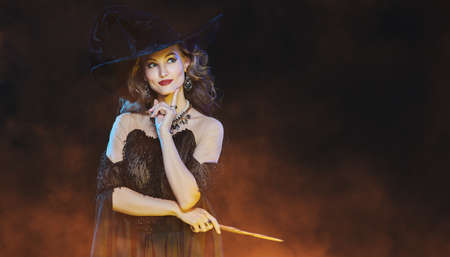 Portrait of a beautiful smiling young witch in a hat and with a magic wand. Halloween celebration, party. Copy space.の写真素材