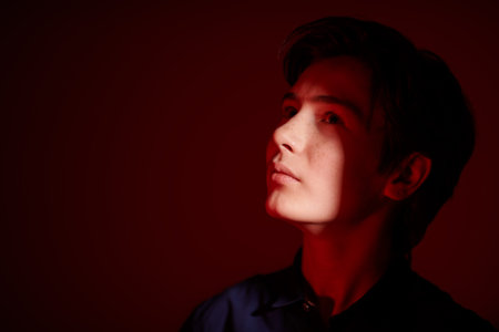 Portrait of a serious handsome boy teenager standing in the dark in red light and looking away...