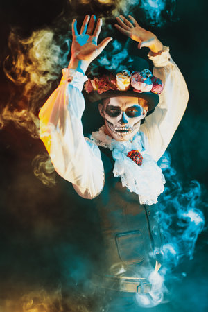 Handsome man in traditional Mexican costume with sugar skull make-up is dancing on a black...
