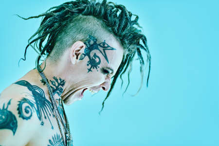 Sideview portrait of an expressive punk rock musician fiercely screaming. Youth alternative culture. Studio portrait on a blue background with copy space.の写真素材