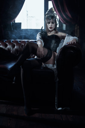 Attractive brunette woman in a black corset and stockings allures on a leather sofa in an expensive...