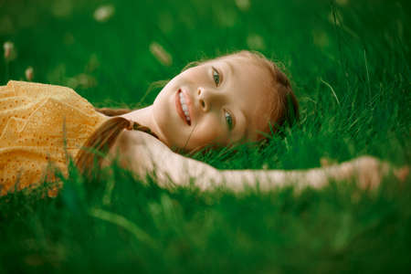 Happy smiling little girl with pigtails lying on a green lawn and enjoying nature. Happy summer child. Rest in the park.の写真素材