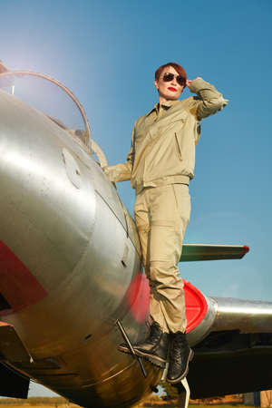 Military and commercial aircraft. Full length portrait of a confident pilot woman wearing uniform and sunglasses standing on her fighter jet ready to fly.の写真素材