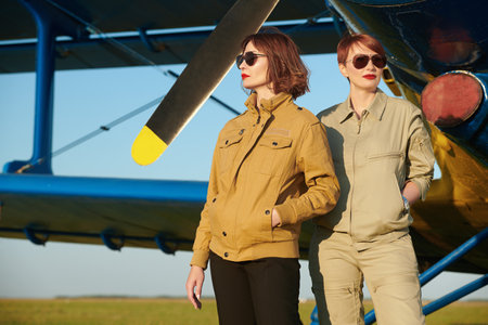 Aviation. Two professional female commercial aviation pilots in uniform and sunglasses stand in front of their plane at the airfield.の写真素材