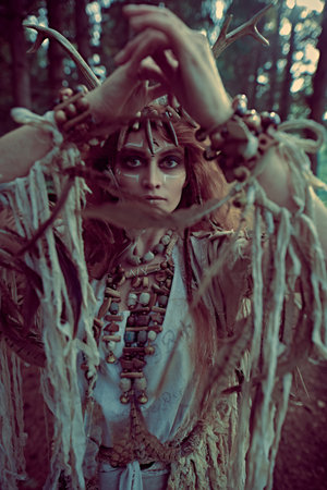 A mystical woman shaman in ethnic dress and deer antlers headdress performs a ritual dance in the...