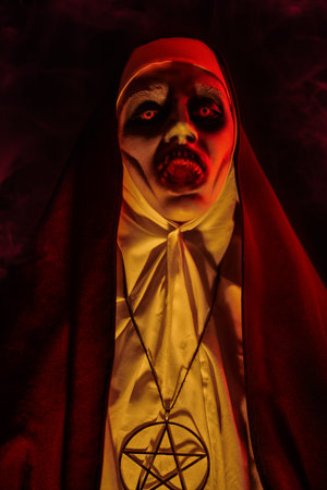 Portrait of a devilish scary nun with bloody teeth standing in candlelight. Halloween and Horrors.