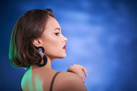 Beauty and jewelry. Portrait of a stunning brunette girl with evening makeup and earrings with gemstones looking alluringly over her shoulder. Copy space.の写真素材