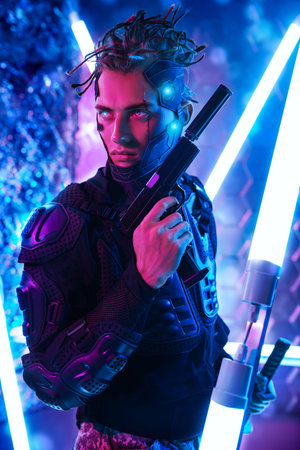 Courageous cyberpunk warrior in a protective costume poses with a gun in his hand standing among...
