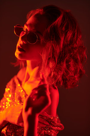 Attractive girl in sparkling top, and stylish glasses with beautiful curly hairstyle alluring in red light. Night party. Disco style.の写真素材